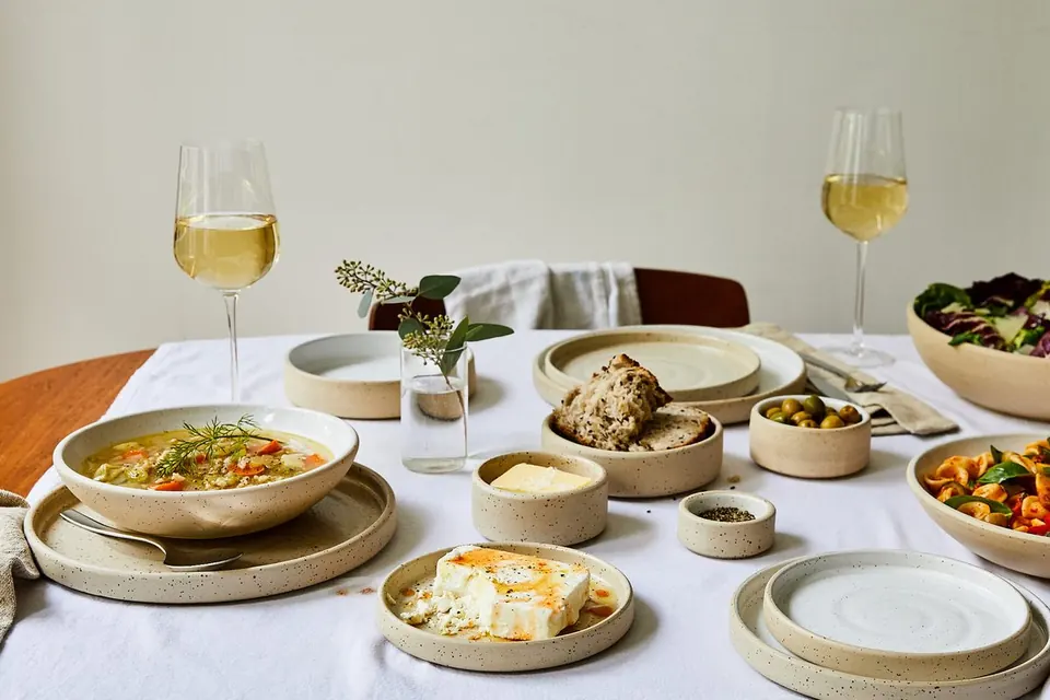 A table set with Sofia Ceramics plates and bowls, food and white wine