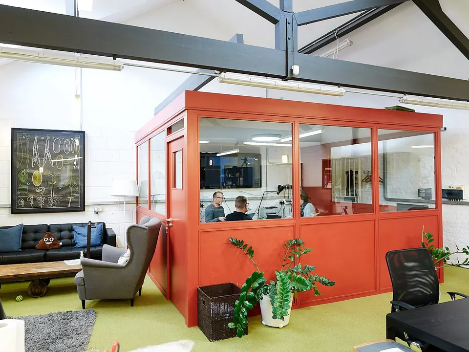 Bright coworking space with an orange glass meeting pod, armchairs and plants