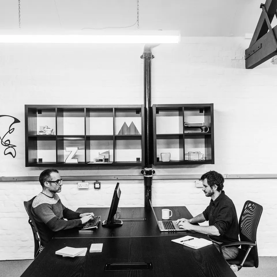 Two people working at a shared desk, in black and white