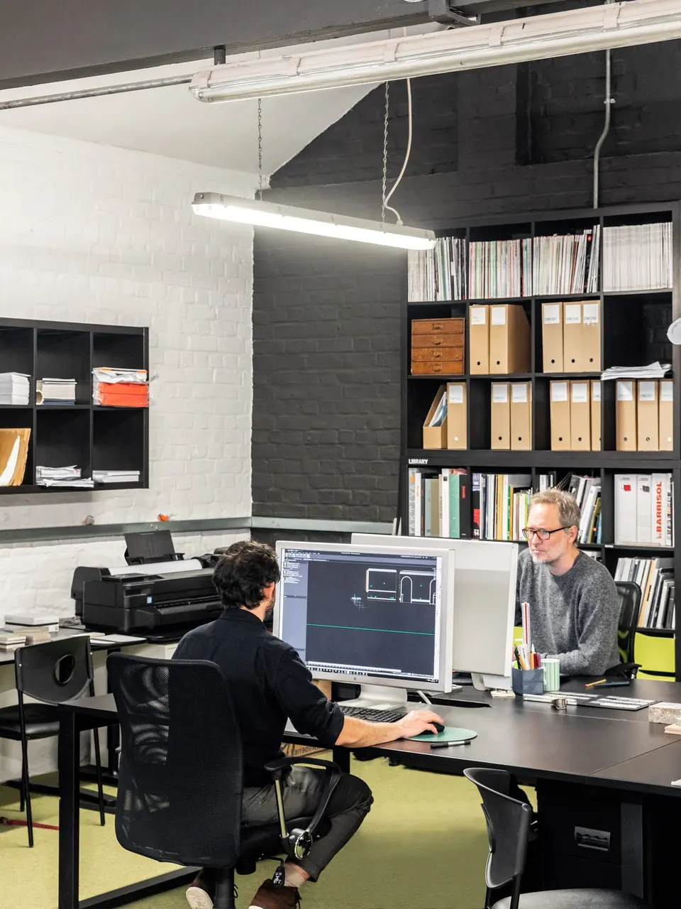 Two people working at desks in front of tall bookshelves