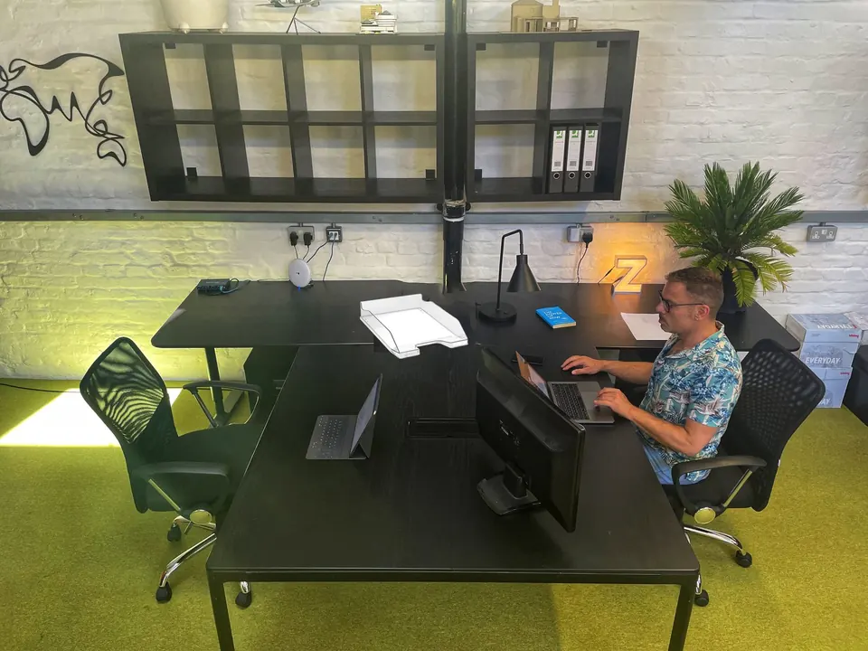 A large L-shaped desk with monitor, lamp and plants